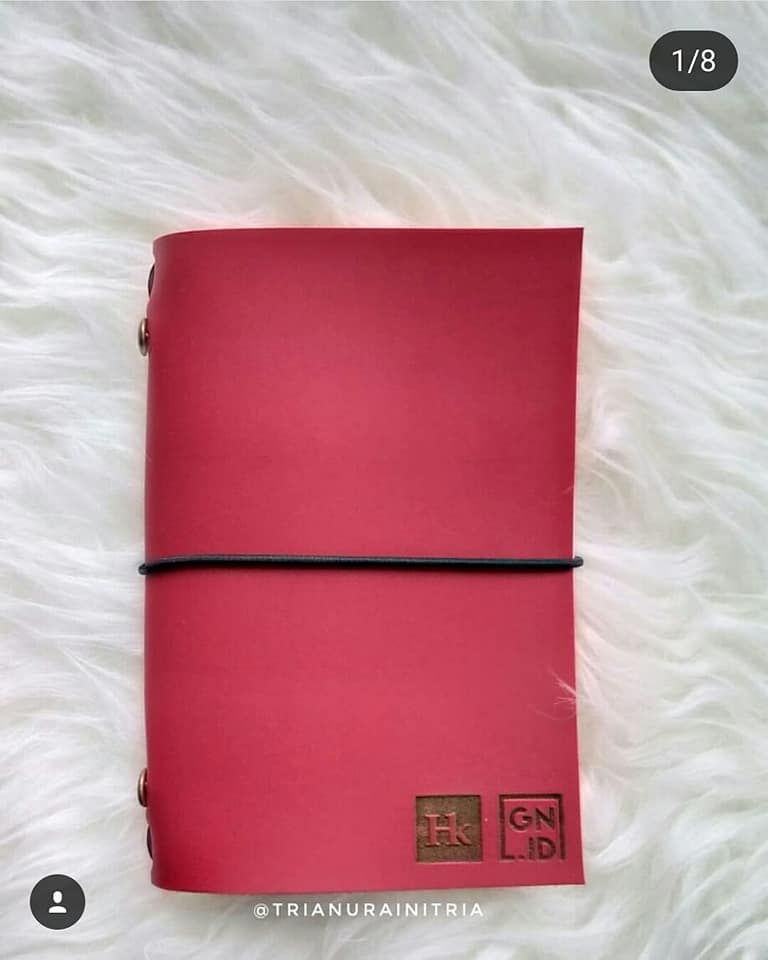 Jurnal kulit Hibrkraft kustom berwarna merah dengan logo ganda untuk GN.ID, diletakkan di atas permukaan kain putih yang lembut.