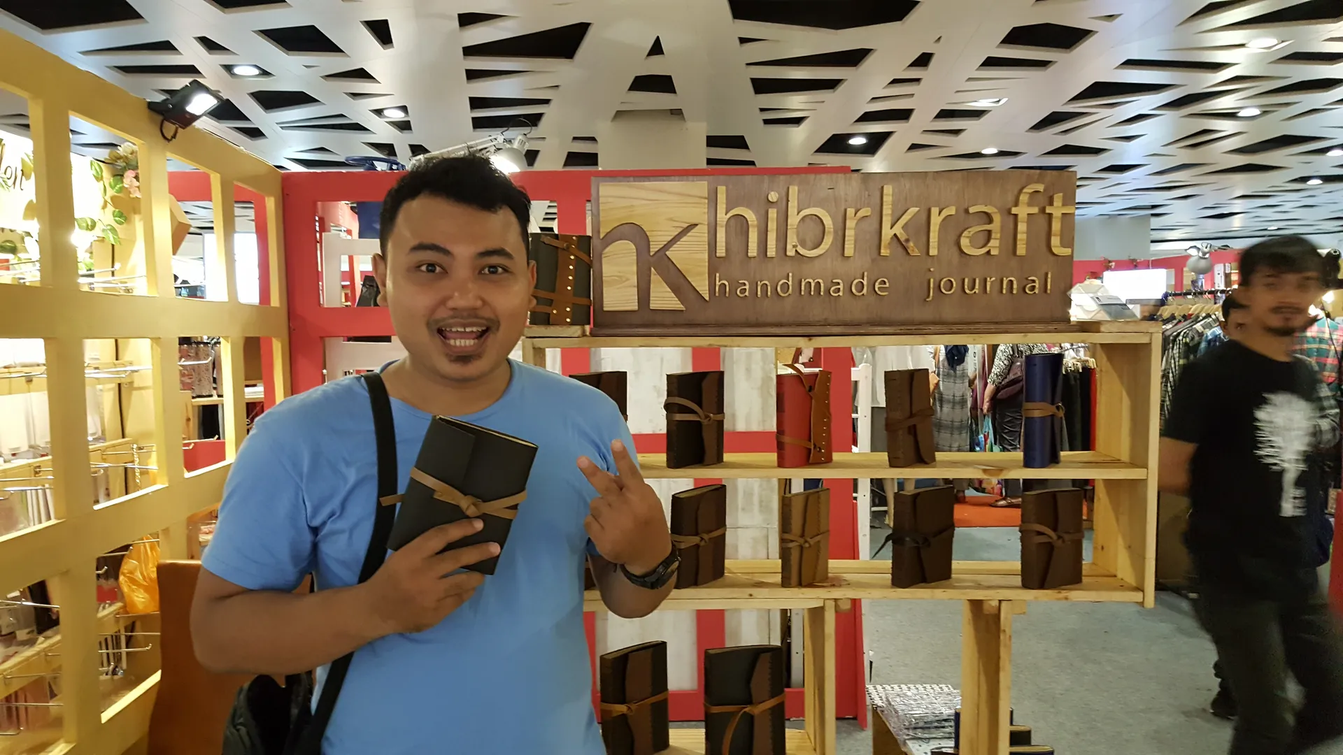 Pendiri Hibrkraft dengan antusias menunjukkan jurnal kulit buatannya di sebuah booth pameran.