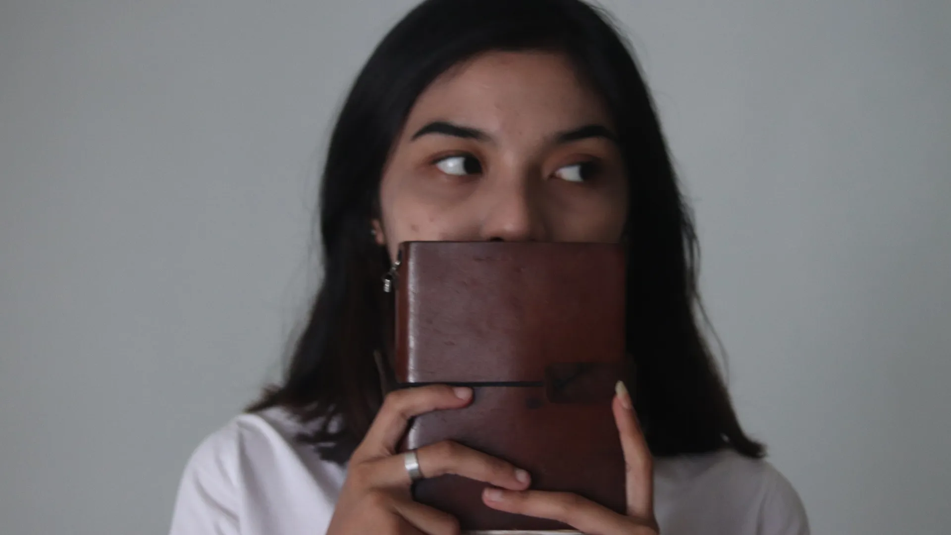 Seorang wanita memegang jurnal kulit berwarna cokelat klasik di depan wajahnya, menyoroti tekstur dan ketahanan materialnya.
