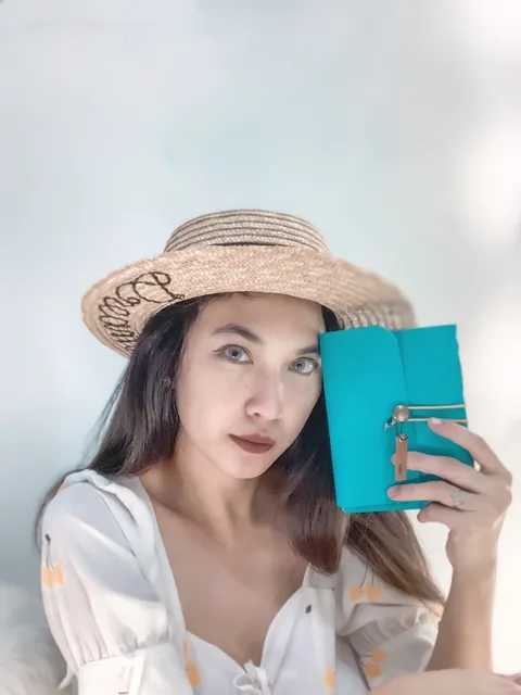 Seorang wanita dengan topi jerami dan pakaian modern memegang jurnal kulit berwarna teal, menunjukkan bagaimana kulit beradaptasi dengan gaya kontemporer.