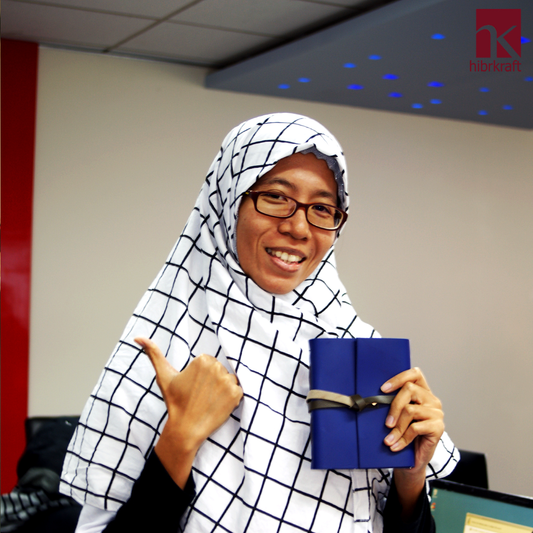 A woman in a pink cardigan and white shirt holding a classic brown leather wrap journal gently with both hands